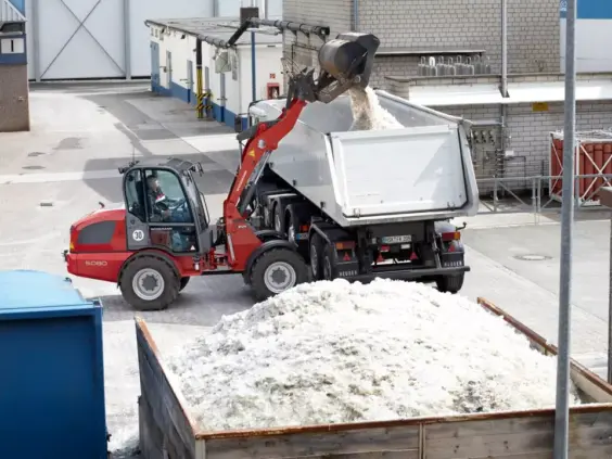 En rød Weidemann Hjullaster 5080 laster hvitt materiale inn i en lastebil.