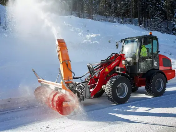 En rød Weidemann Hjullaster 5080 fjerner snø med en stor snøfreser på en vintervei.