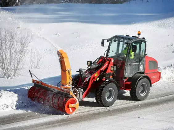 En rød Weidemann Hjullaster 5080 med snøfreser rydder en snødekket vei om vinteren.
