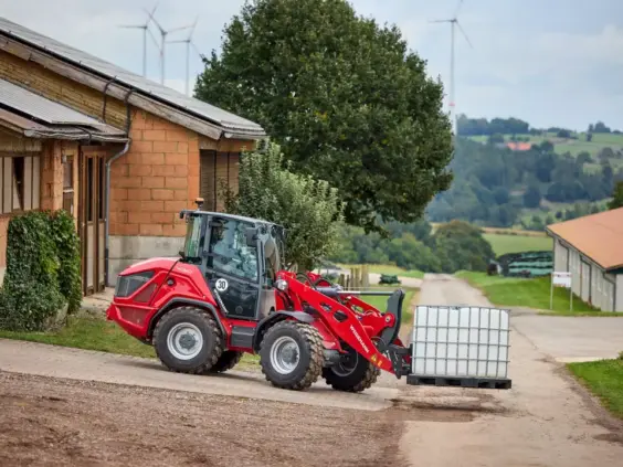 Rød Weidemann Hjullaster 4060 som transporterer en hvit plastbeholder på en gårdsvei.