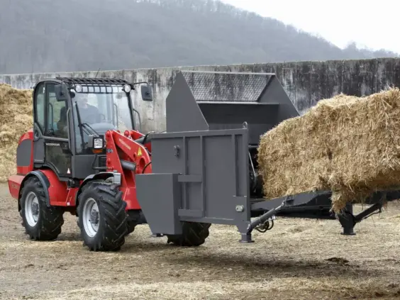 En rød Weidemann Hjullaster 3080 i arbeid med en halmspreder på en gård.