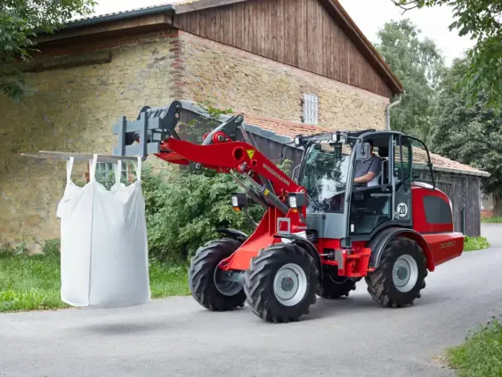 En rød Weidemann Hjullaster 3080 løfter en stor hvit sekk på en gårdsvei.