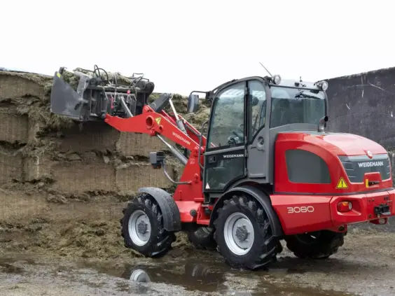 En rød Weidemann Hjullaster 3080 i arbeid med fôr på en gård.