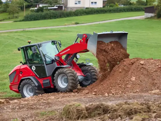 Rød Weidemann Hjullaster 3060 tipper jord på en haug i et grønt landskap.