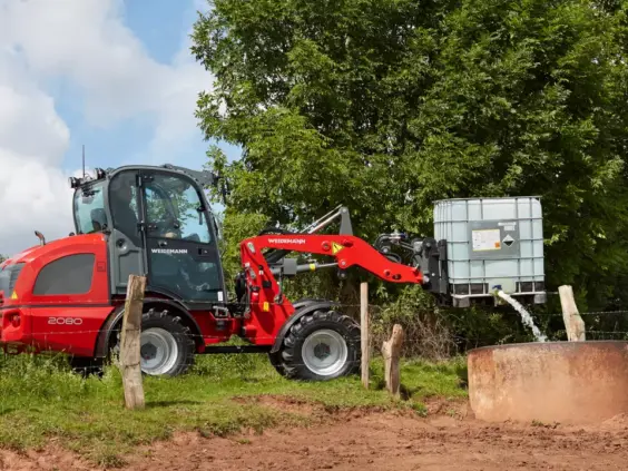 Rød Weidemann Hjullaster 2080 tømmer en vanntank i en kum utendørs.