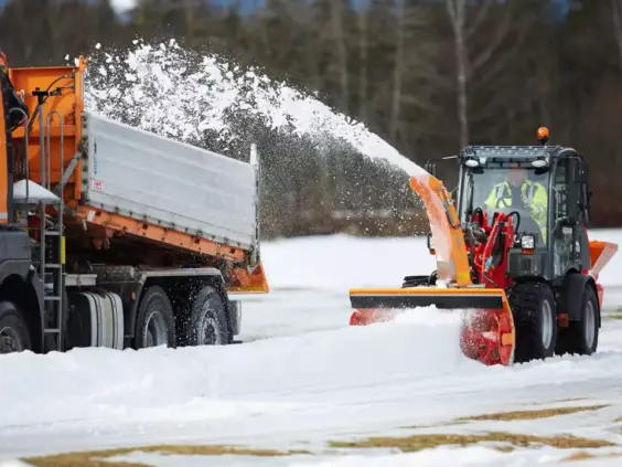 Weidemann Hjullaster 2080 med snøfreser som laster snø på en oransje lastebil.