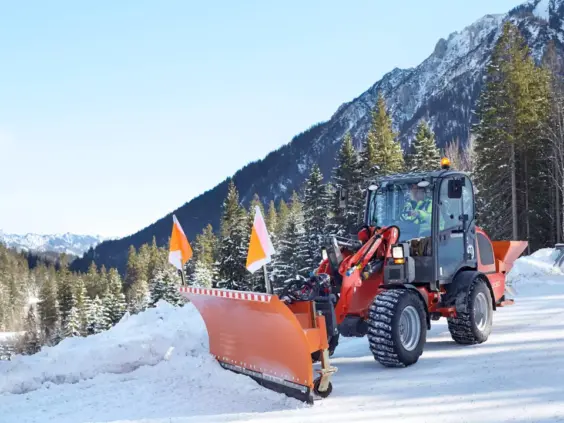 En rød Weidemann Hjullaster 2080 brøyter snø på en vei i fjellet.