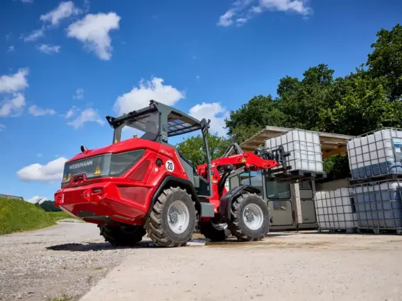 En rød Weidemann Hjullaster 2060 som løfter en hvit vanntank utendørs.