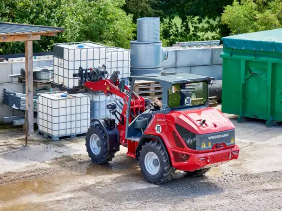 En rød Weidemann Hjullaster 2060 løfter en hvit IBC-beholder på en grusplass.