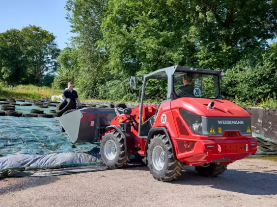 En rød Weidemann Hjullaster 2060 i arbeid på en gård med bildekk.