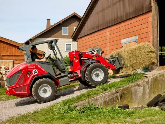 En rød Weidemann Hjullaster 2060 som transporterer en høyball på en gård.