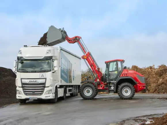 En rød Weidemann 9580T teleskopisk hjullaster laster organisk materiale i en hvit lastebil.