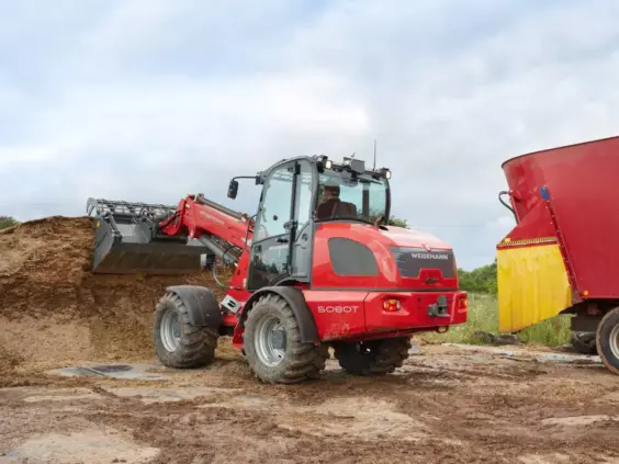 En rød Weidemann 5080T teleskopisk hjullaster som arbeider ved en stor fôrhaug.