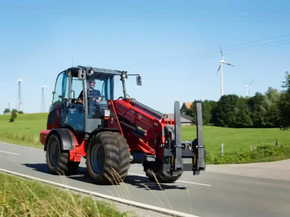 Rød Weidemann 4080T teleskopisk hjullaster som kjører på en vei i et grønt landskap.