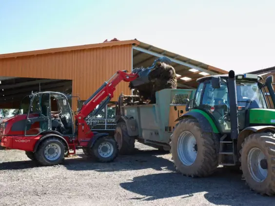 En rød Weidemann 4080T teleskopisk hjullaster laster fôr inn i en tilhenger.