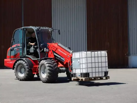 En rød Weidemann 4080T teleskopisk hjullaster som løfter en hvit tank på en pall.
