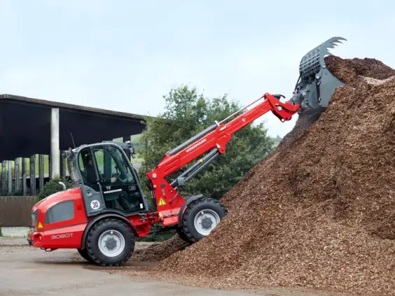 En rød Weidemann 3080T teleskopisk hjullaster i arbeid med en stor haug flis.