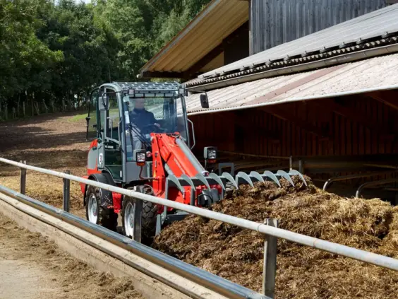 En rød Weidemann 3080T teleskopisk hjullaster som flytter gjødsel ved en låve.