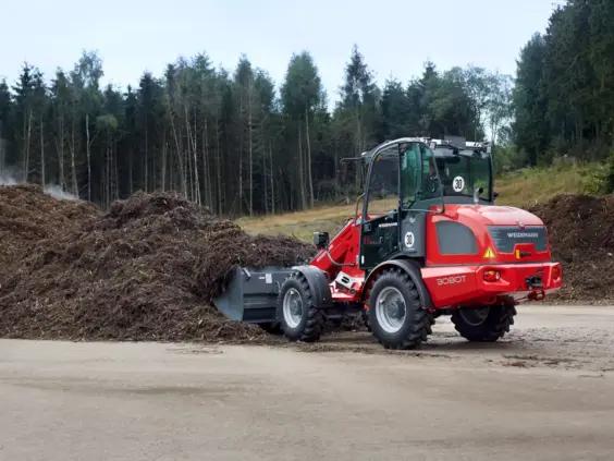 En rød Weidemann 3080T teleskopisk hjullaster i arbeid med en stor komposthaug.