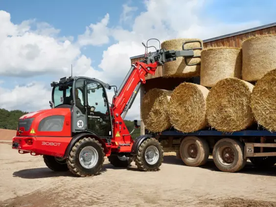 Weidemann 3080T teleskopisk hjullaster som løfter store rundballer av halm på en gård.