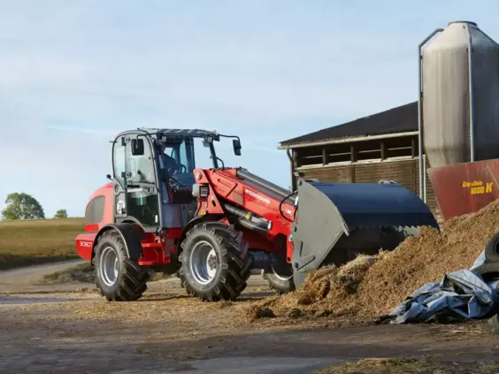 Rød Weidemann 3080T teleskopisk hjullaster med skuffe på en gård.