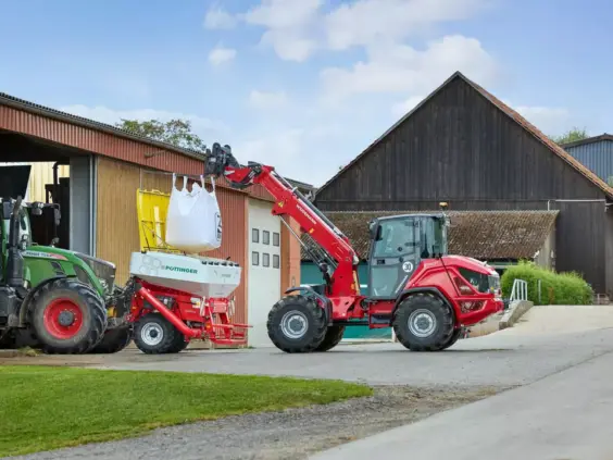 En rød Weidemann 3060T teleskopisk hjullaster løfter en storsekk på et gårdsbruk.