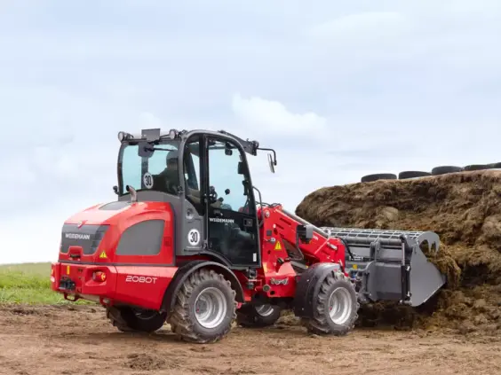 En rød Weidemann 2080T teleskopisk hjullaster i arbeid ved en silohaug.