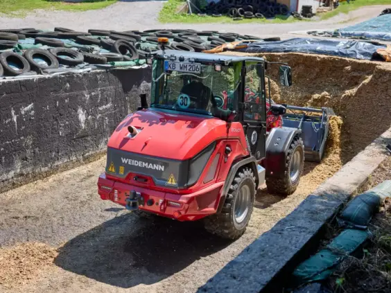 En rød Weidemann 2060T teleskopisk hjullaster i arbeid med fôr i en plansilo.