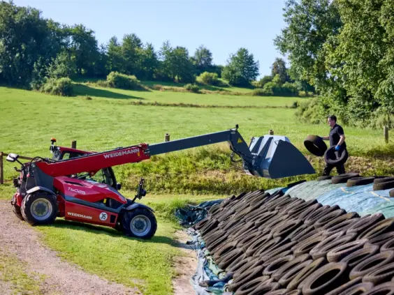 Rød Weidemann teleskoplaster T6025 i arbeid ved en silohaug på en gård.