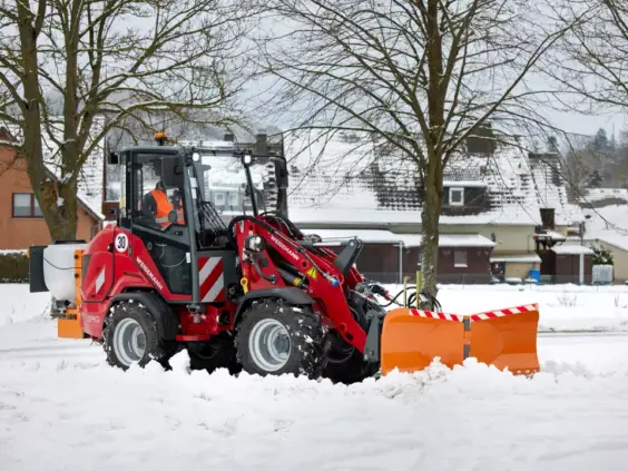 Weidemann Hoftrac 1390 hjullaster rydder snø med et oransje plogskjær.