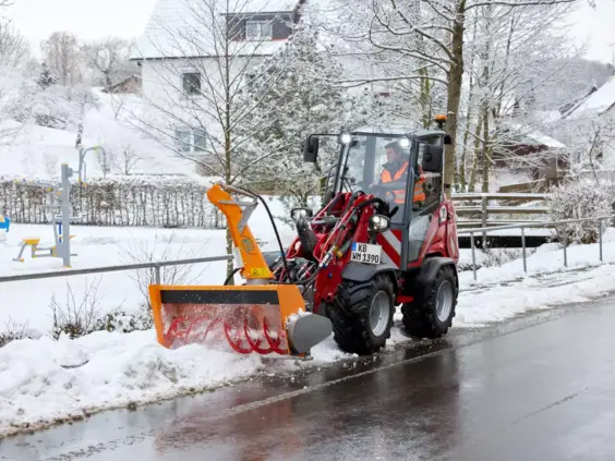 En rød Weidemann Hoftrac 1390 fjerner snø fra veien med en snøfreser.