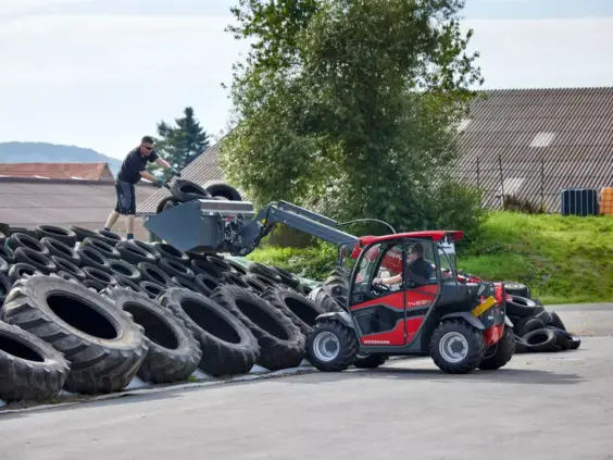 Rød Weidemann teleskoplaster T4512e som flytter dekk sammen med en arbeider.
