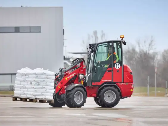 En rød Weidemann Hoftrac 1290e elektrisk minilaster som frakter hvite sekker på en pall.
