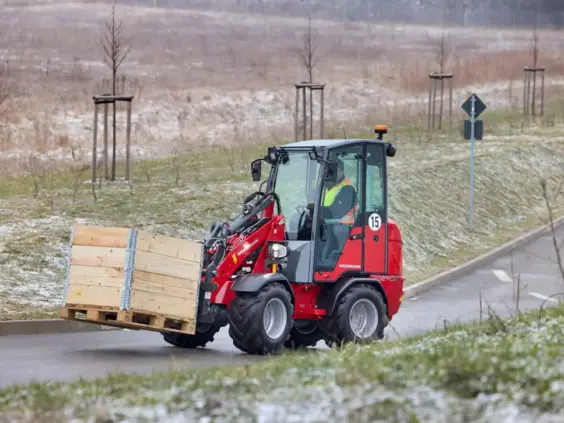 Rød Weidemann Hoftrac 1290e elektrisk minilaster som transporterer en trekasse på en vei.