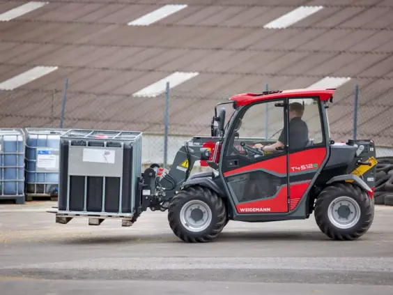 En rød Weidemann teleskoplaster T4512e som løfter en IBC-beholder utendørs.