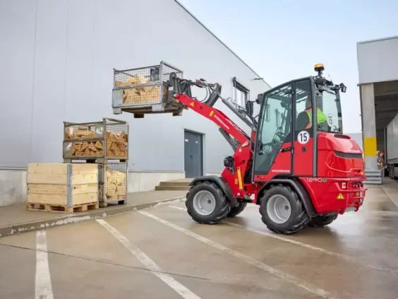 En rød Weidemann Hoftrac 1290e elektrisk minilaster som løfter en kasse med ved.