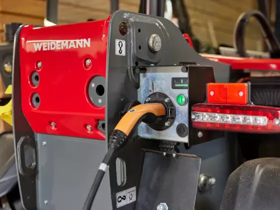 Lading av en elektrisk Weidemann teleskoplaster T4512e med en oransje ladekabel.