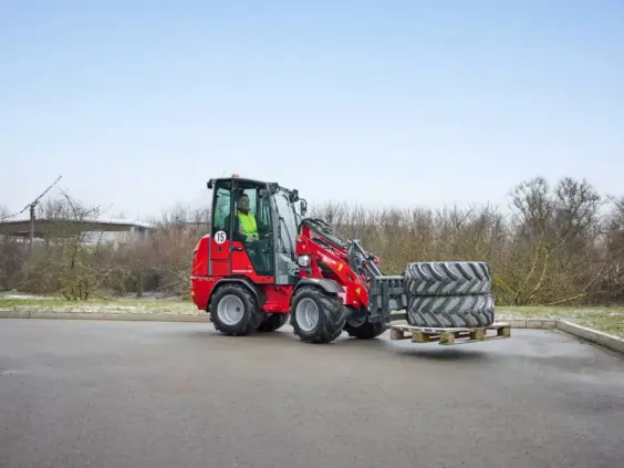 Rød Weidemann Hoftrac 1290e elektrisk minilaster som transporterer store dekk på en pall.