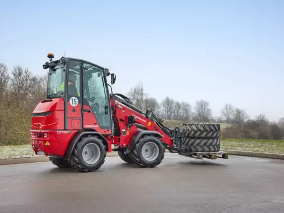 Rød Weidemann Hoftrac 1290e elektrisk minilaster som transporterer store dekk på en pall.