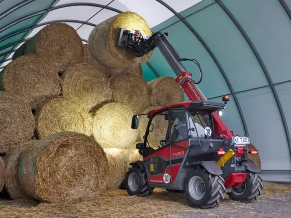 En rød Weidemann teleskoplaster T4512 løfter en rundballe i en tunnelhall.