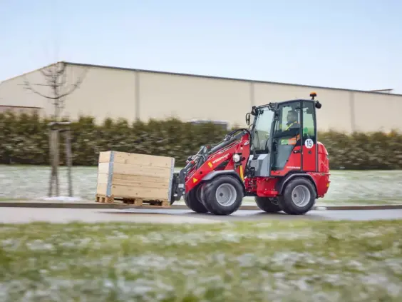 En rød Weidemann Hoftrac 1290e elektrisk minilaster som transporterer en trekasse utendørs.