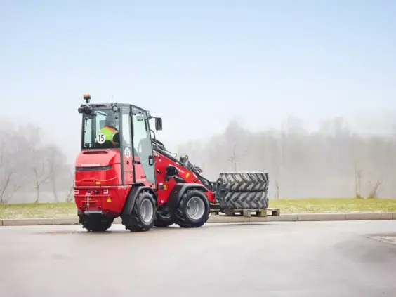 Rød Weidemann Hoftrac 1290e elektrisk minilaster som transporterer store dekk på en pall utendørs.