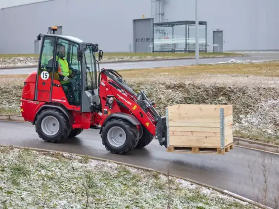 Rød Weidemann Hoftrac 1290e elektrisk minilaster som transporterer en stor trekasse utendørs.