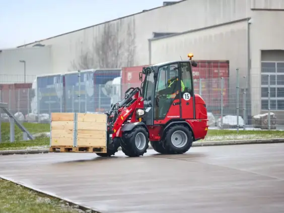 En rød Weidemann Hoftrac 1290e elektrisk minilaster som transporterer en trekasse på en pall.