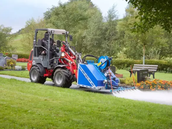 Weidemann Hoftrac 1280 minilaster med spyleutstyr rengjør en gangvei på en gravlund.