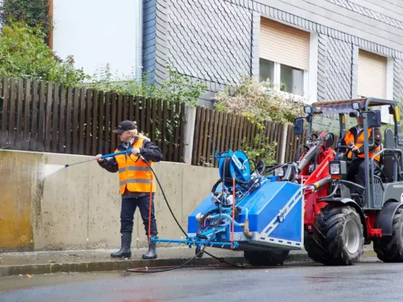 En arbeider høytrykksspyler en murvegg ved siden av en Weidemann Hoftrac 1280 minilaster.