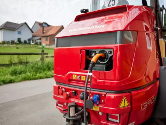 En rød Weidemann Hoftrac 1390e elektrisk kompaktlaster under lading utendørs.