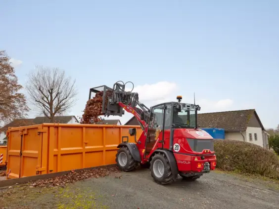 En rød Weidemann Hoftrac 1260LP minilaster tømmer løv i en stor oransje container.