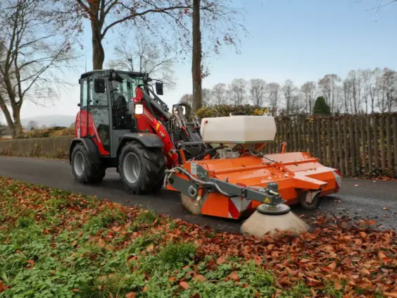 Rød Weidemann Hoftrac 1260LP minilaster utstyrt med feiemaskin som fjerner høstløv på asfalten.