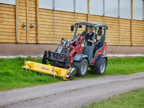 En rød Weidemann Hoftrac 1260LP minilaster klipper gresset med en gul Müthing beitepusser.